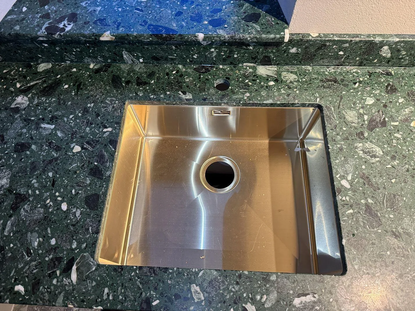 Närbild på underlimmad mässingsfärgad diskho i en matt Terrazzo Verde Alpi köksbänkskiva i Borrby.