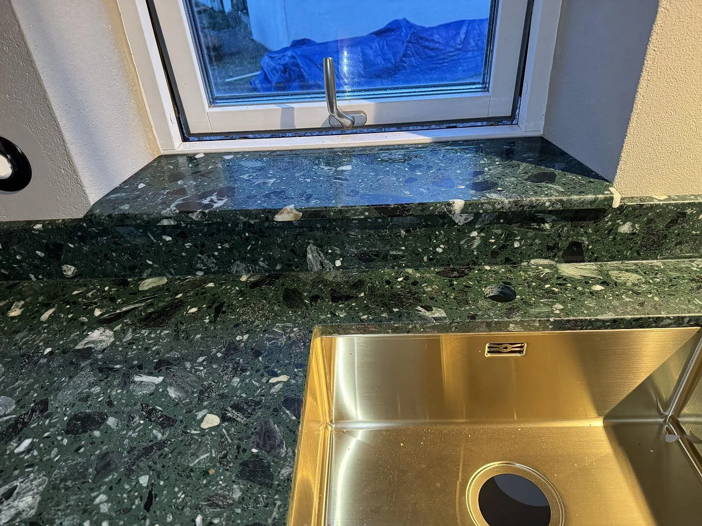Detalj av Terrazzo Verde Alpi i matt utförande med fönsterbänk, låg stänkkant och mässingsfärgad diskho i Borrby.