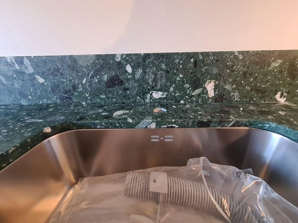 Detalj av rostfri diskho och stänkskydd i en matt Terrazzo Verde Alpi köksbänkskiva i Stockholm.