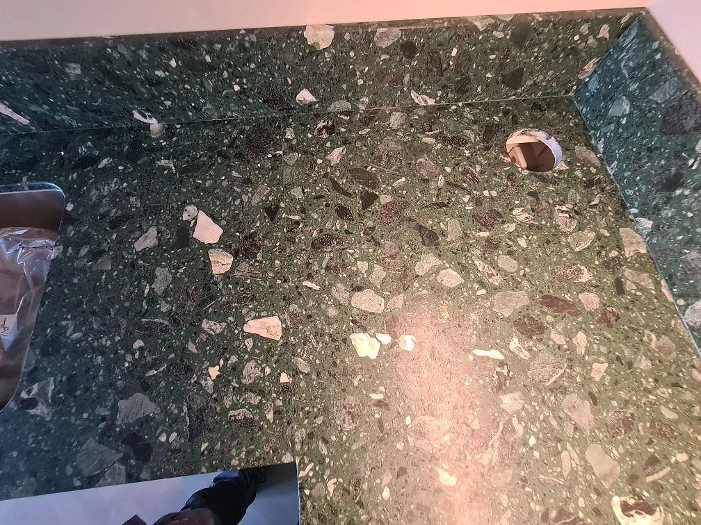 L-formad köksbänkskiva i mörkgrön Terrazzo Verde Alpi, matt, med stänkskydd och blandarhål i ett kök i Stockholm.