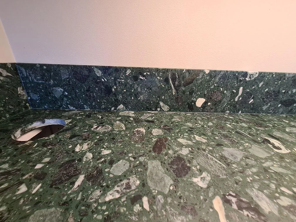 Närbild av grön Terrazzo Verde Alpi, matt, med uppvikt stänkskydd och blandarhål i Stockholm.