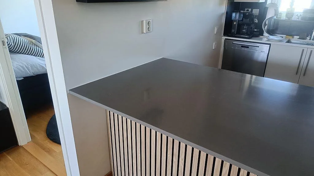 Köksbänkskiva i polerad Technistone Gobi Grey komposit på en halvö med trälamellfront i Växjö.