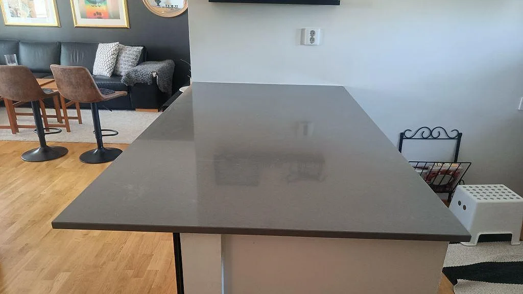 Polerad grå kompositbänkskiva i Technistone Gobi Grey på en kökshalvö i öppen planlösning i Växjö.