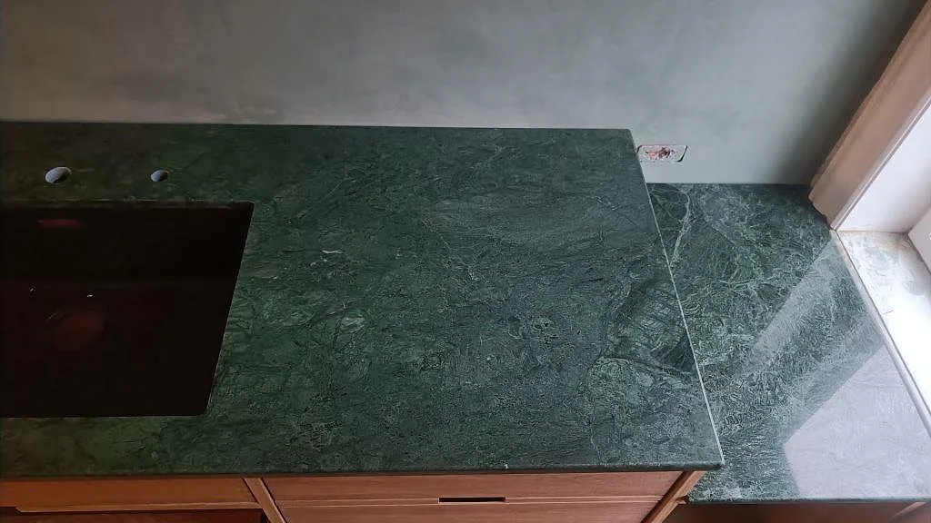 Detalj av polerad Verde Guatemala marmor med svart diskho och intilliggande stenyta vid fönster i Frederiksberg.