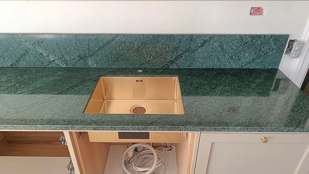 Köksbänkskiva i polerad Verde Guatemala marmor med guldfärgad underlimmad diskho och stänkskydd i Frederiksberg.