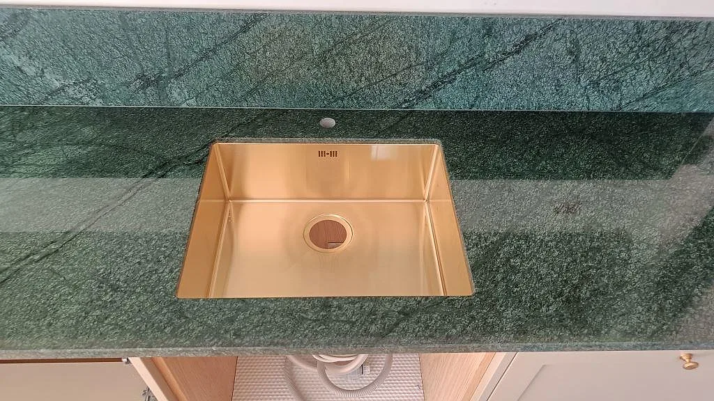 Detaljbild av guldfärgad underlimmad diskho i polerad Verde Guatemala marmorbänkskiva med matchande stänkskydd i Frederiksberg.