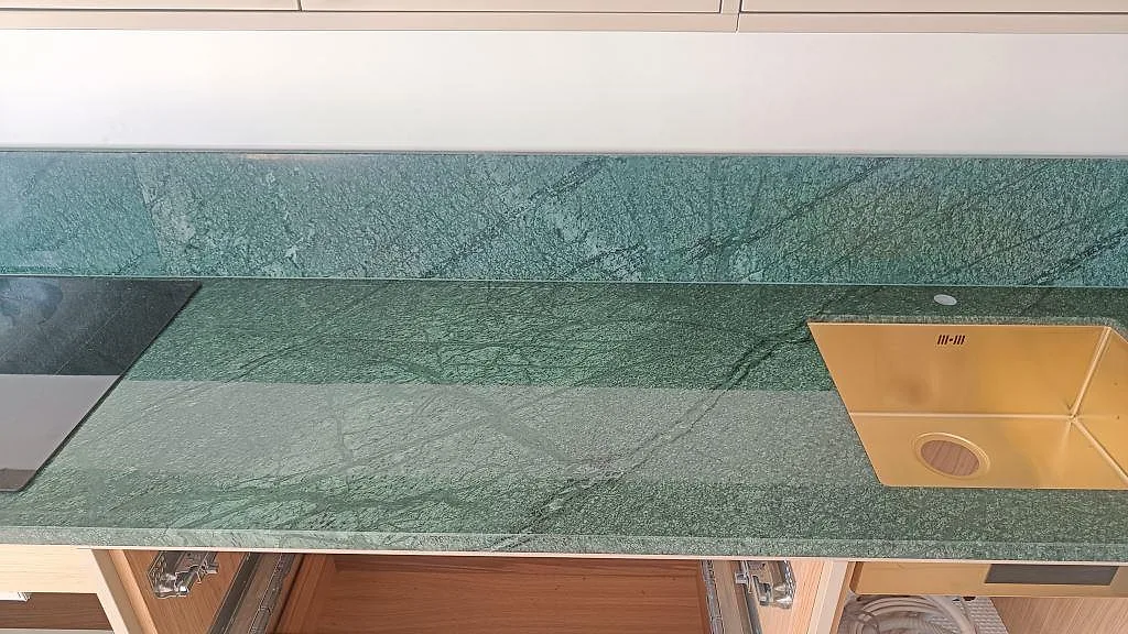 L-formad köksbänkskiva i polerad Verde Guatemala marmor med diskho, svart induktionshäll och uppvikt stänkskydd i Frederiksberg.