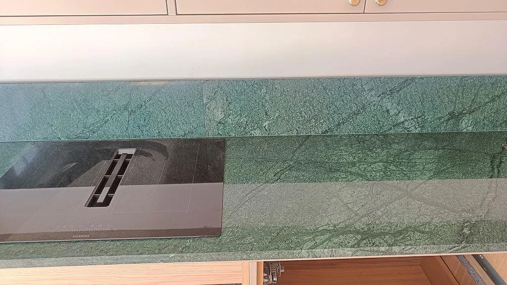 Polerad grön Verde Guatemala marmorbänkskiva med svart induktionshäll och matchande stänkskydd i ett kök i Frederiksberg.