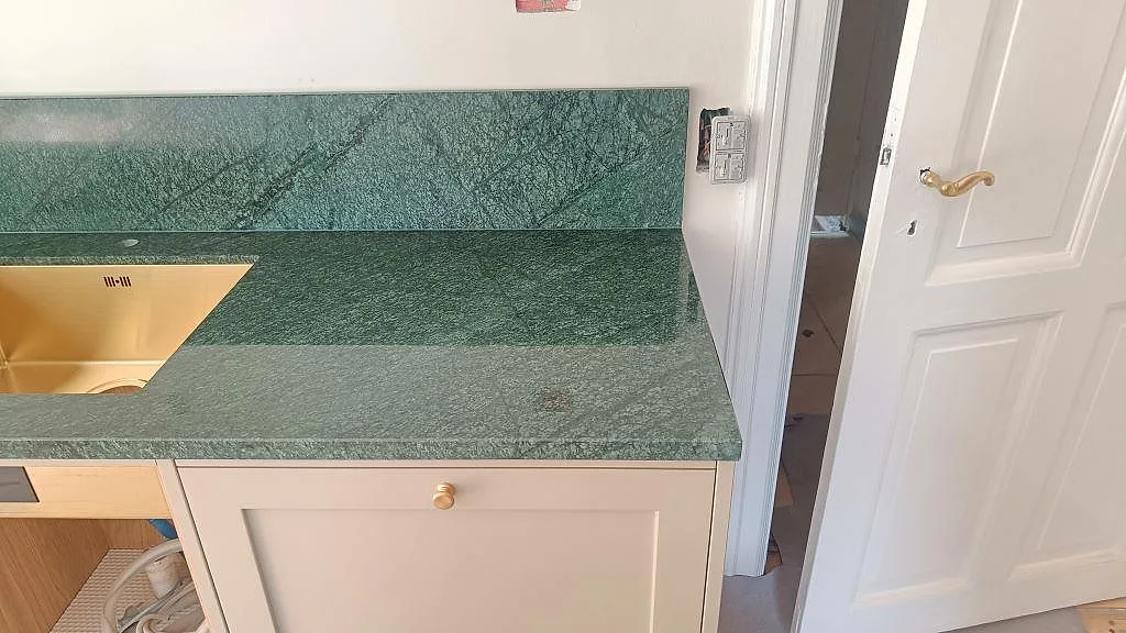 Polerad Verde Guatemala marmorbänkskiva med guldfärgad diskho, grön stänkkant och ljusa köksluckor i Frederiksberg.
