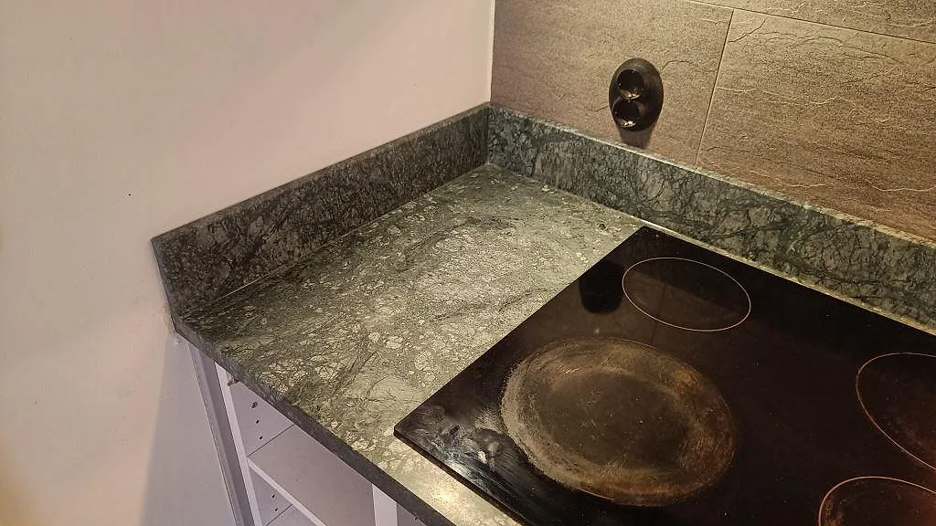 Vänster hörn av matt Verde Guatemala-marmor med låg stänkkant och svart induktionshäll i Göteborg.