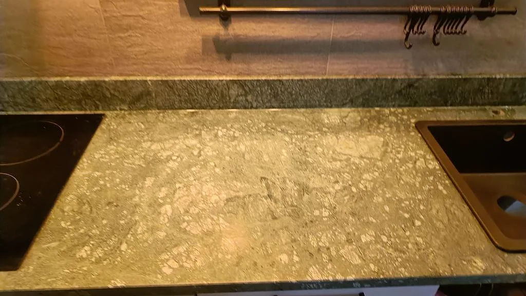 Närbild på matt Verde Guatemala-marmor mellan induktionshäll och diskho i en L-formad köksbänkskiva i Göteborg.