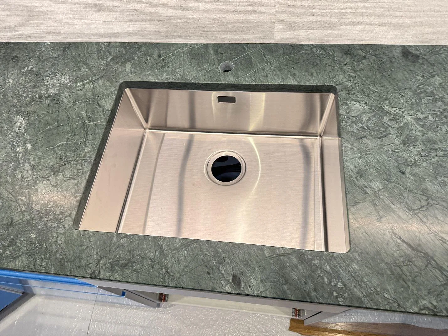 Närbild på rostfri diskho i matt Verde Guatemala-marmor, med blandarhål och grön stenådring i Göteborg.