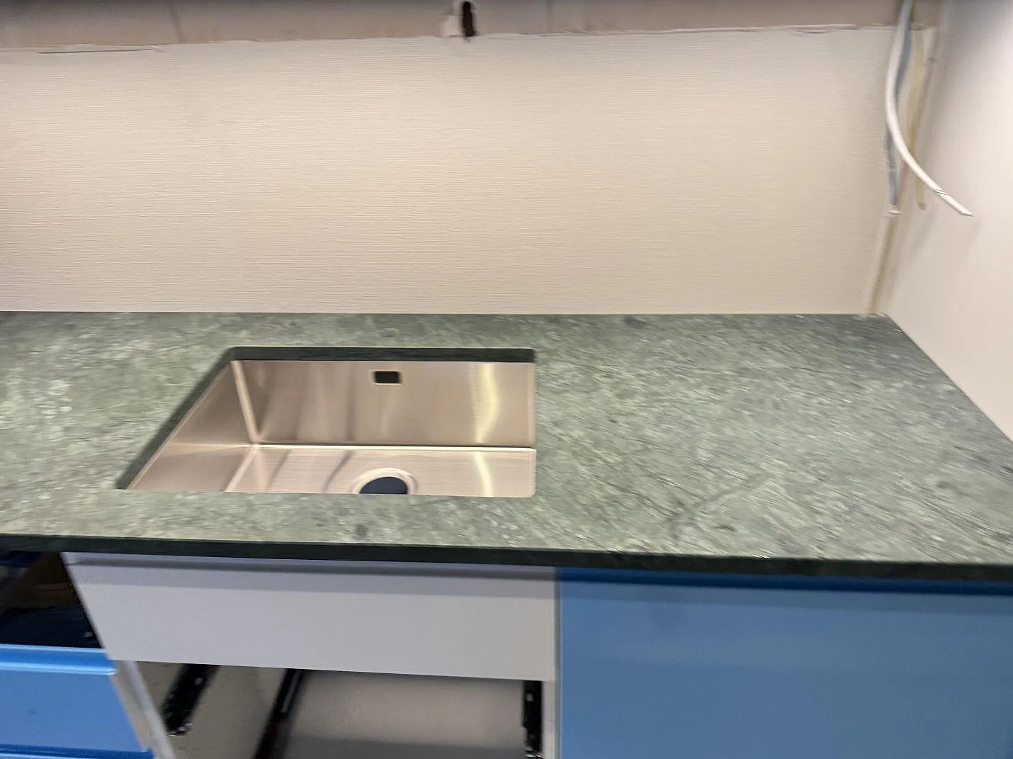 Diskbänksdel i matt Verde Guatemala-marmor med rostfri diskho, tjock stenkant och pågående köksmontering i Göteborg.