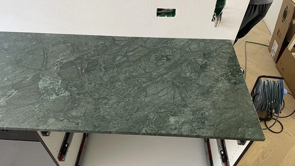 Detalj av polerad Verde Guatemala marmor som köksbänkskiva över öppna stommar under montering i København.