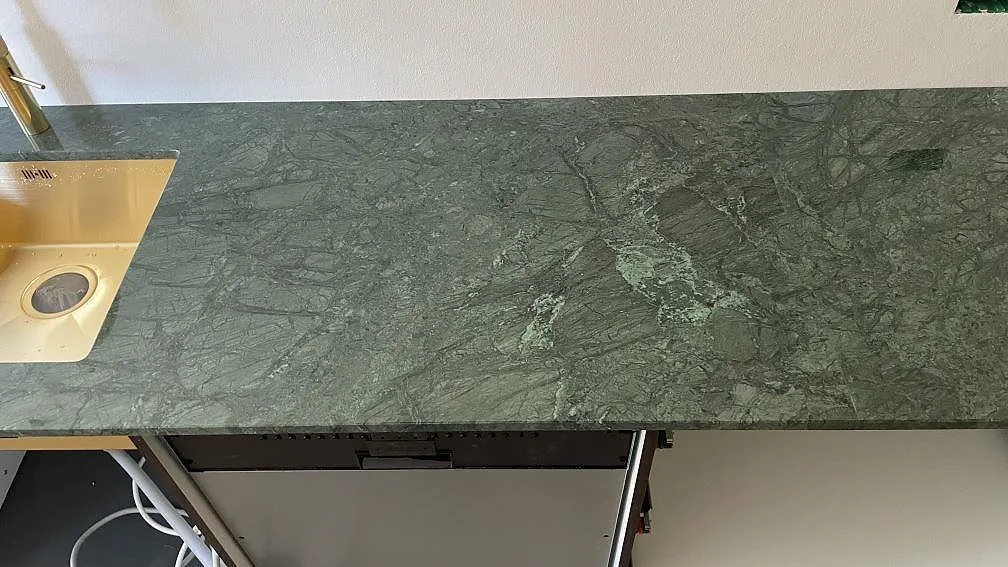 Lång köksbänk i polerad Verde Guatemala marmor med synlig diskhozon och grön ådring i København.