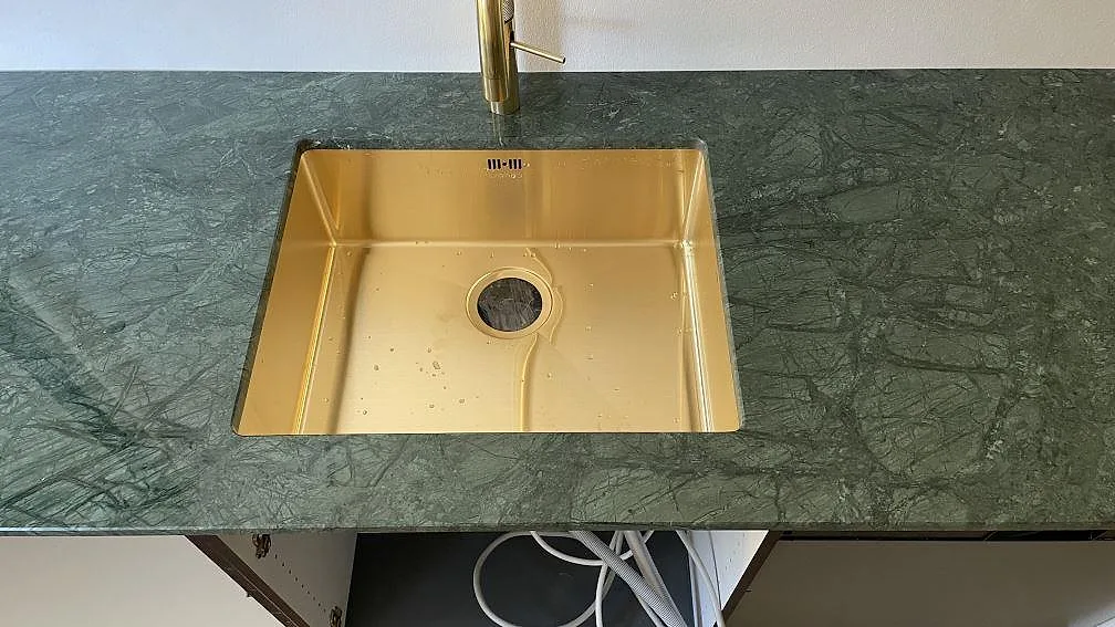 Närbild på polerad Verde Guatemala marmor med guldfärgad diskho och mässingsfärgad blandare i København.