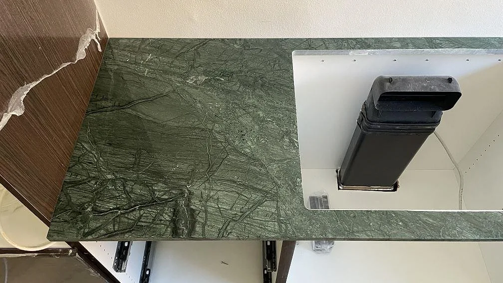 Köksbänkskiva i polerad Verde Guatemala marmor med urtag och öppna köksstommar under montering i København.