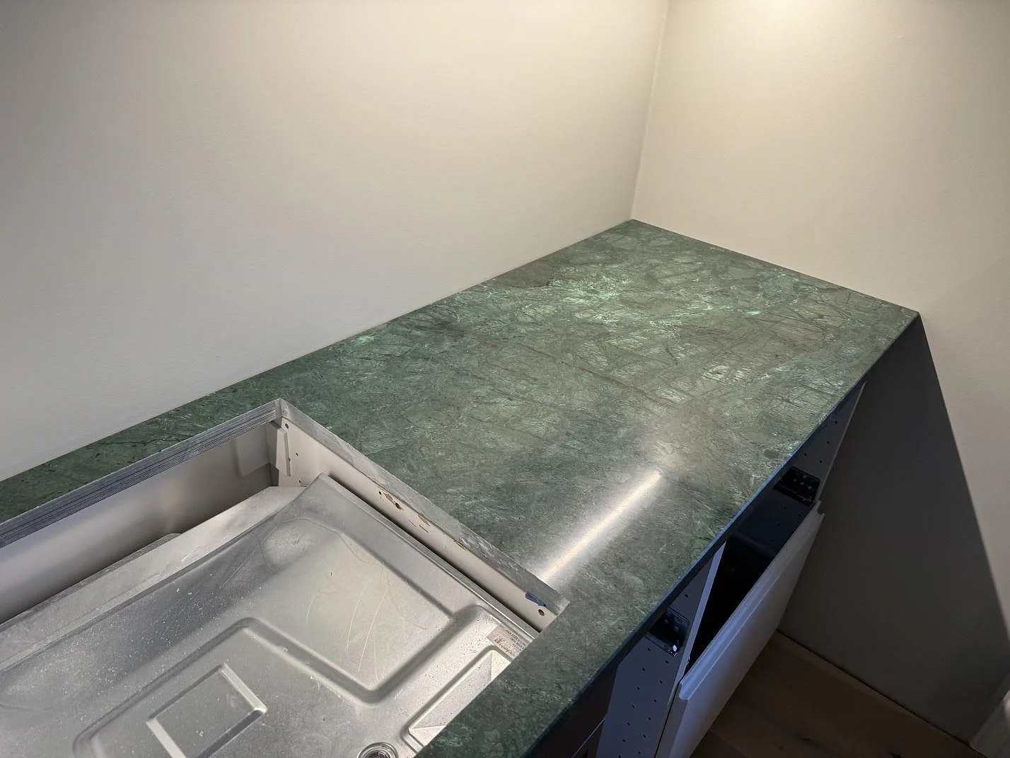 Detalj av polerad Verde Guatemala marmor runt vitvaruöppning och vit köksstomme i Limhamn.