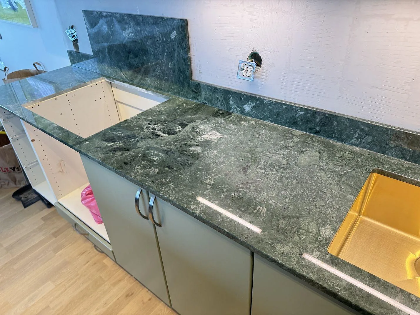 Köksbänkskiva i grön Verde Guatemala-marmor, polerad, med kraftig vit ådring och öppna köksstommar i ett kök under montering i Limhamn.