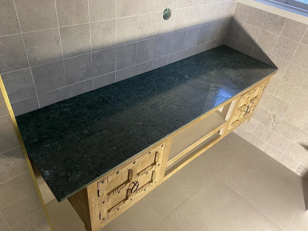 Bänkskiva i mörkt grön Verde Guatemala natursten, polerad, monterad ovanpå ett snickrat sideboard i ek mot kaklad vägg i Lund.