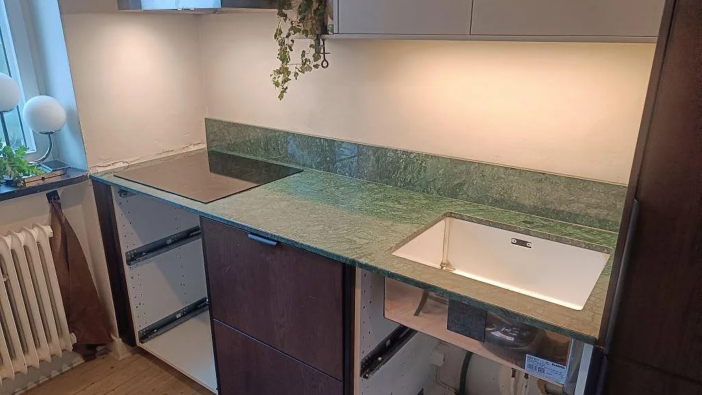 Köksbänkskiva i polerad Verde Guatemala marmor med vit underlimmad diskho, induktionshäll och uppvikt stänkkant i Malmö.