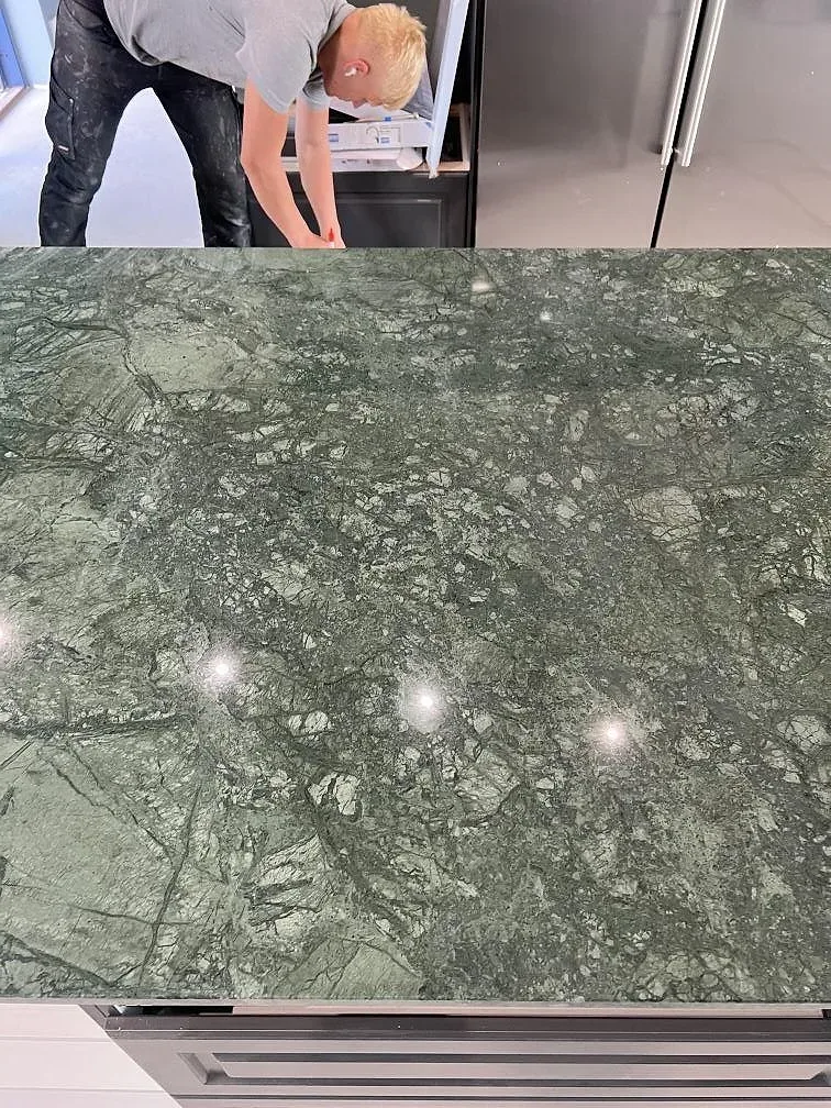 Närbild av polerad Verde Guatemala marmor på köksö där den gröna ådringen syns under montering i Nässjö.