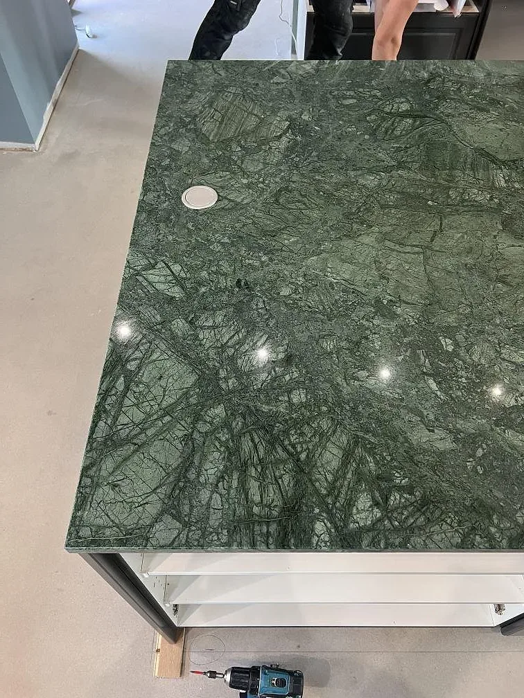 Detalj av polerad Verde Guatemala marmor på köksö med kabelgenomföring och mörka stommar i Nässjö.