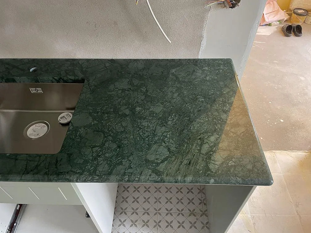 Närbild på polerad Verde Guatemala bänkskiva med rostfri diskho, blandarhål och grön marmorådring i Staffanstorp.