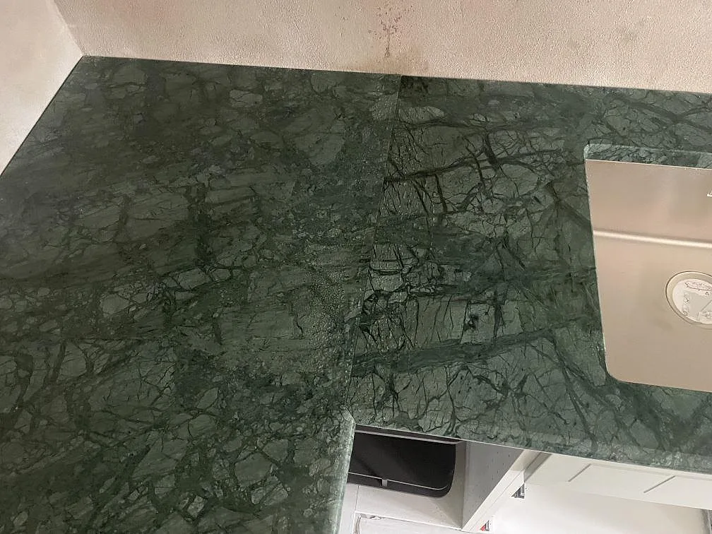 Detalj av polerad Verde Guatemala marmorbänkskiva med skarv, diskho och mörkgrön stenstruktur i Staffanstorp.
