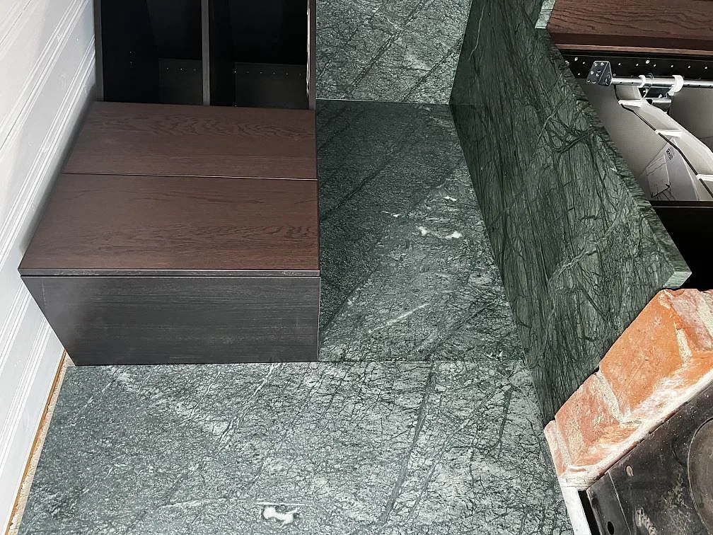 Detalj av matt Verde Guatemala marmor som bänkskiva och uppvikt kant mot mörka trästommar och tegel i Svedala.
