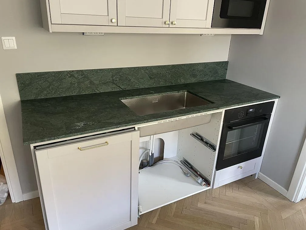 Köksbänkskiva i grön Verde Guatemala marmor, matt, med rostfri diskho och låg stänkkant i ett kök under montering i Uppsala.