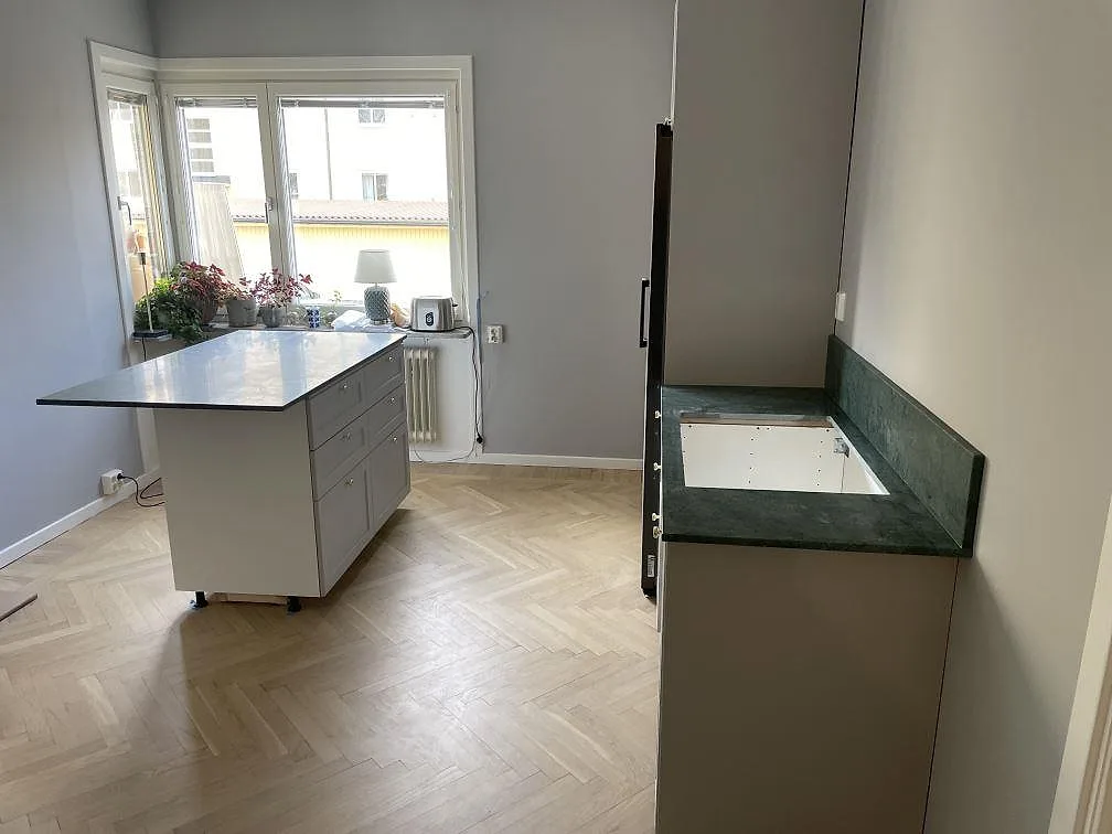 Kök i Uppsala under montering med grön marmorbänkskiva i Verde Guatemala på väggsidan och en ljus fristående köksyta i rummet.