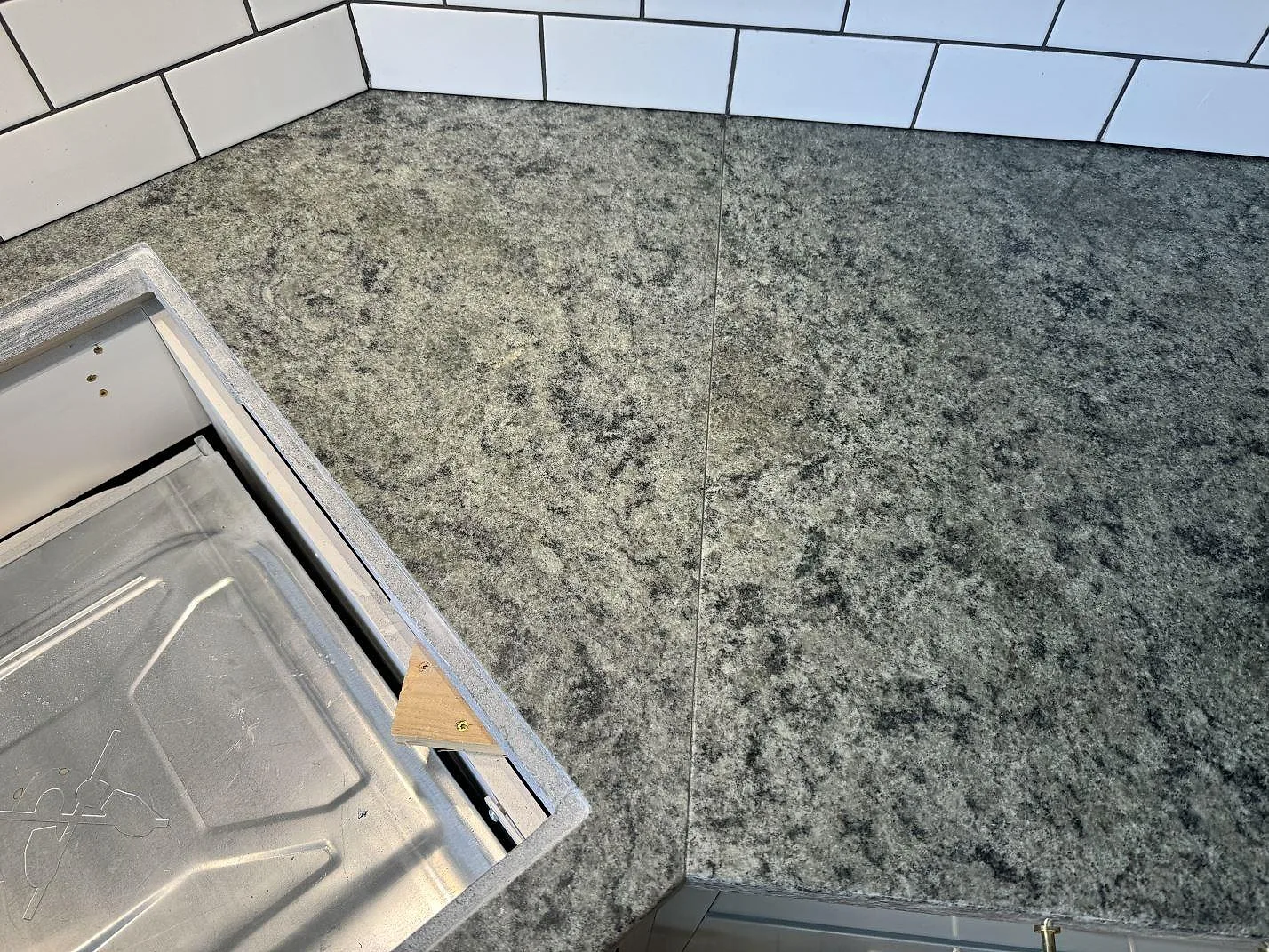 Närbild av grågrön Verde Savana granit över köksbänk med hällöppning och vit kakelvägg i Bunkeflostrand.