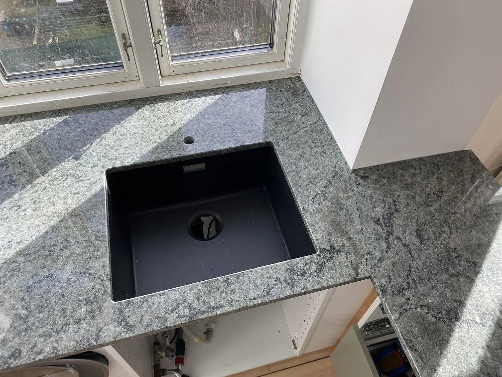 Polerad köksbänkskiva i Verde Savana granit med mörk diskho och anslutande bänkyta vid fönster i Frederiksberg Danmark.