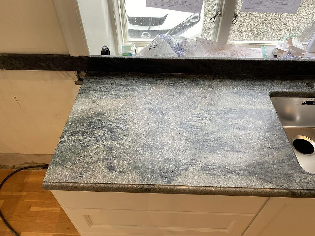 Detalj av matt Verde Savana granit med blandarhål, diskho och uppvikt stänkkant i Harlösa.