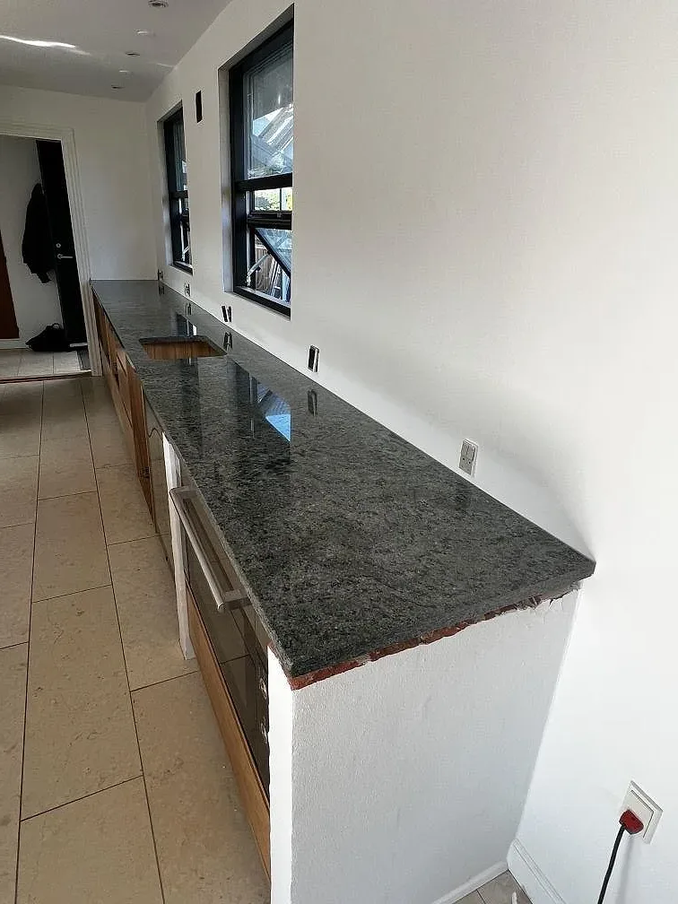Installerad Verde Savana granit längs en vit vägg med stora fönster och blank polerad yta i ett kök i Hellerup.