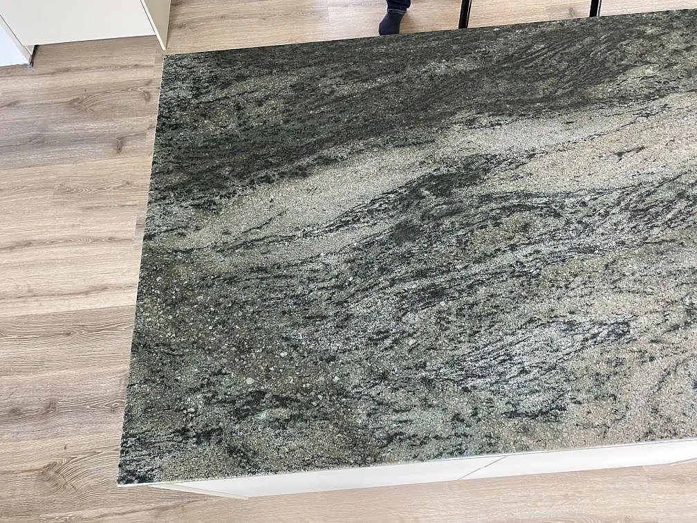 Närbild av polerad Verde Savana granit på köksön i Kävlinge, med gröngrå ådring och ljusa mineralstråk.