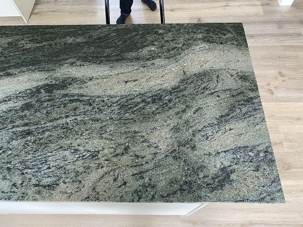Stor yta av polerad Verde Savana granit på köksö i Kävlinge, med mörka vågiga mönster över bänkskivan.