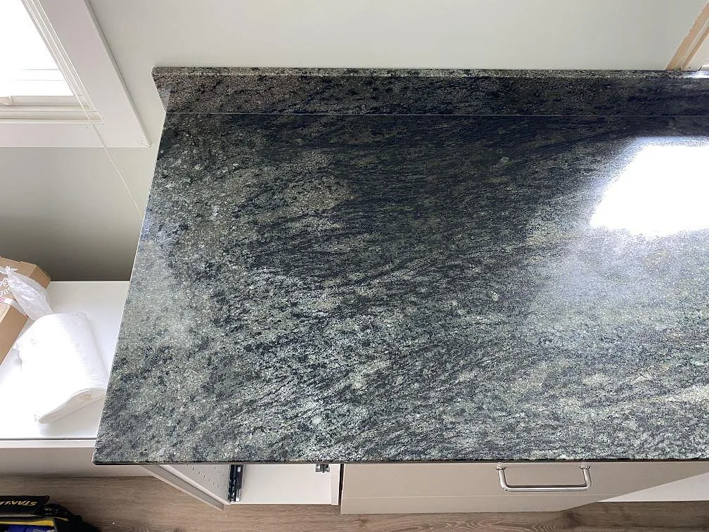 Polerad Verde Savana granit som bänkskiva vid fönster i Kävlinge, med blank yta och låg stänkkant mot väggen.