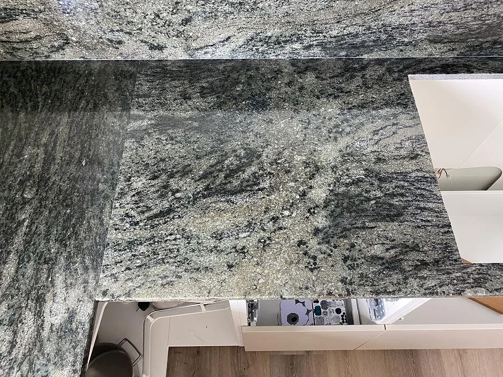 Detalj av polerad Verde Savana granit i Kävlinge, där bänkskiva och stänkkant möts med tydlig ådring.