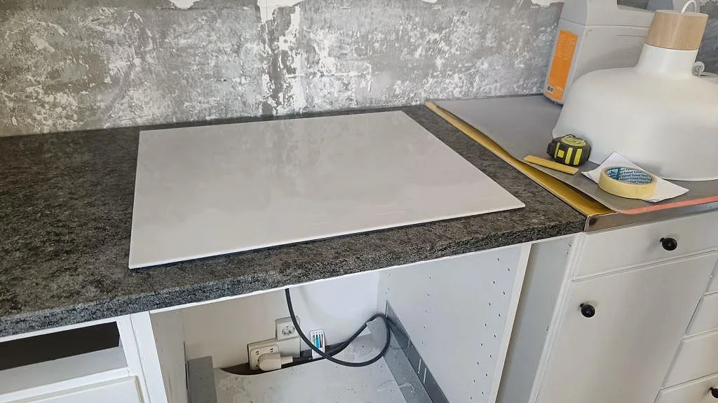 Detalj av polerad köksbänkskiva i Verde Savana granit med induktionshäll i ett kök under montering i Landskrona.
