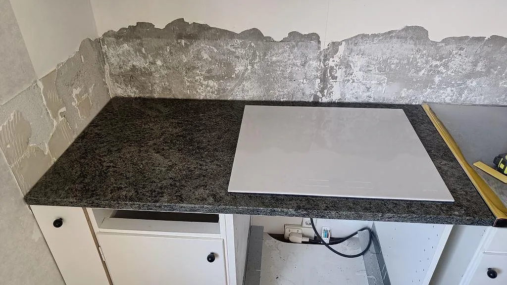 Köksbänkskiva i Verde Savana granit, polerad, med plats för en induktionshäll i ett kök under montering i Landskrona.