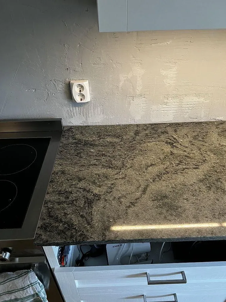 Detalj av polerad Verde Savana granit vid svart induktionshäll och LED-belyst vägg i ett kök i Limhamn.