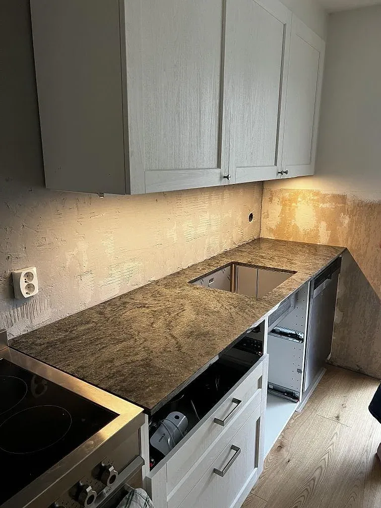 Köksbänkskiva i polerad Verde Savana granit, 20 mm, med diskhoöppning i ett vitt shakerkök i Limhamn under montering.