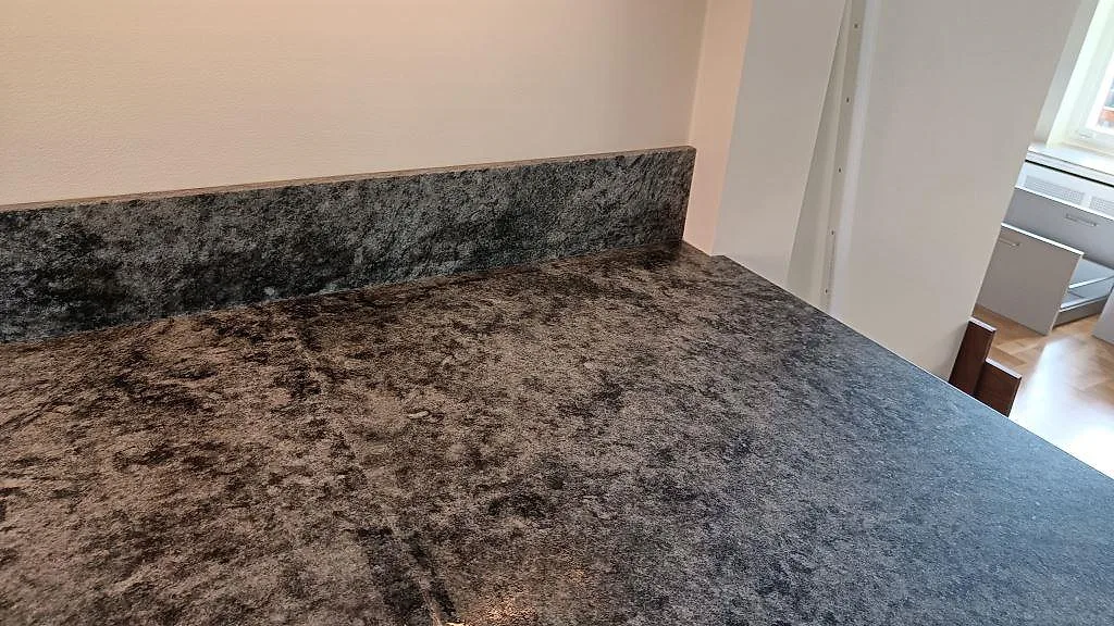 Uppvikt stänkkant och arbetsyta i matt Verde Savana granit längs köksväggen i Limhamn.