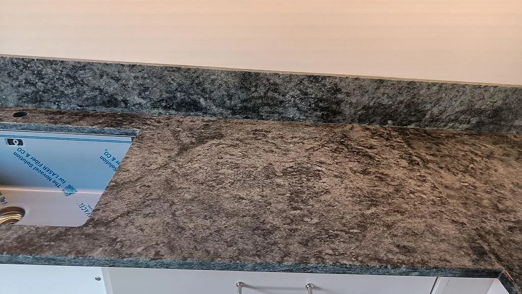 Närbild av diskho, blandarhål och stänkkant i matt Verde Savana granit i Limhamn.