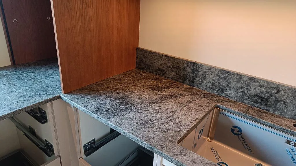 Hörndetalj vid diskhon med matt Verde Savana granit och stänkkant intill träinredning i Limhamn.