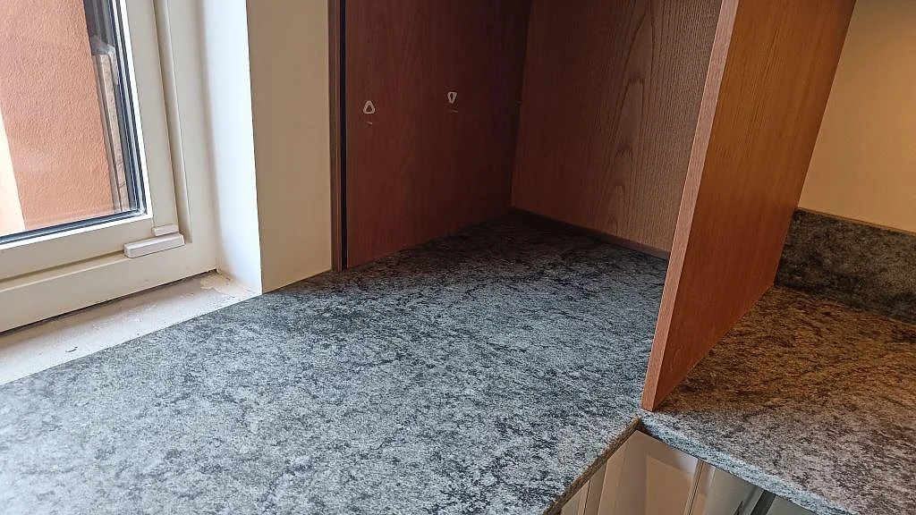 Matt Verde Savana granit runt fönster och högskåp med matchande stänkkant i ett kök i Limhamn.