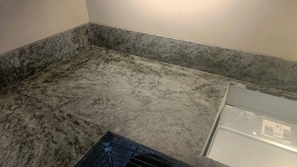Ovanifrån av Verde Savana granitbänk i hörn med uppvikt stänkkant i samma gröngrå sten i ett kök i Malmö.