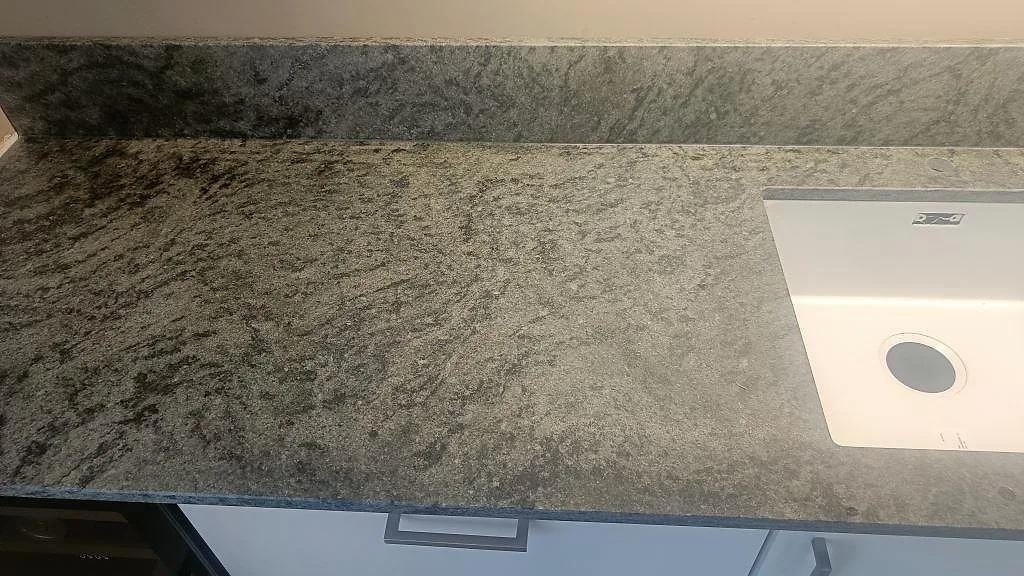 Matt Verde Savana granitbänk med underlimmad vit diskho och låg stänkkant i samma sten i ett kök i Malmö.